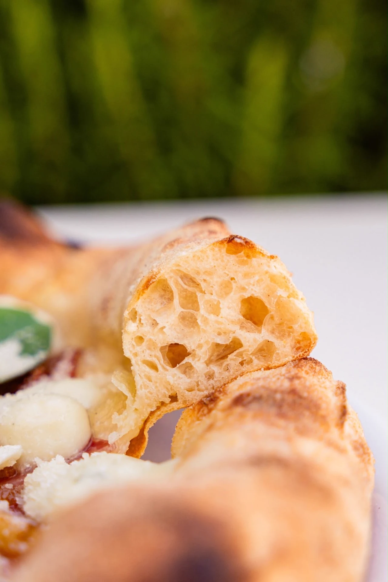 Grande plano do interior da borda da pizza, com alvéolos abertos resultantes da longa fermentação